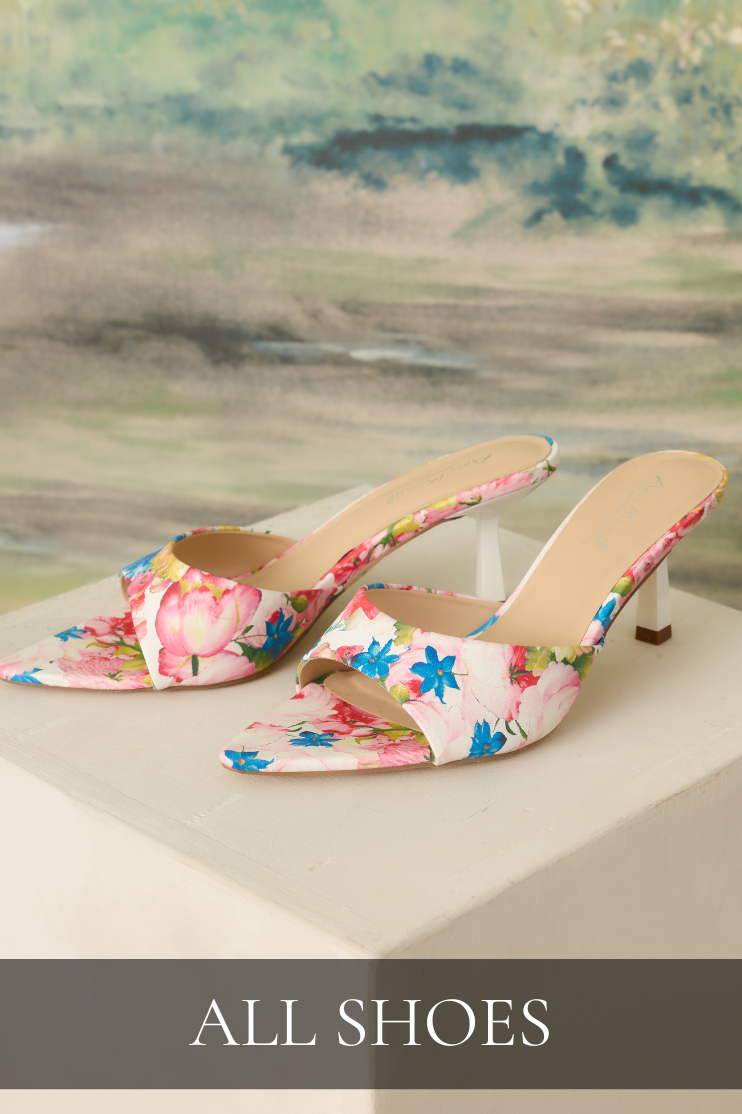 Showcasing a pair of pointed toe floral mule heels with white kitten heels displayed on a pedestal, promoting the women’s shoe collection with bright spring florals and elegant styling.