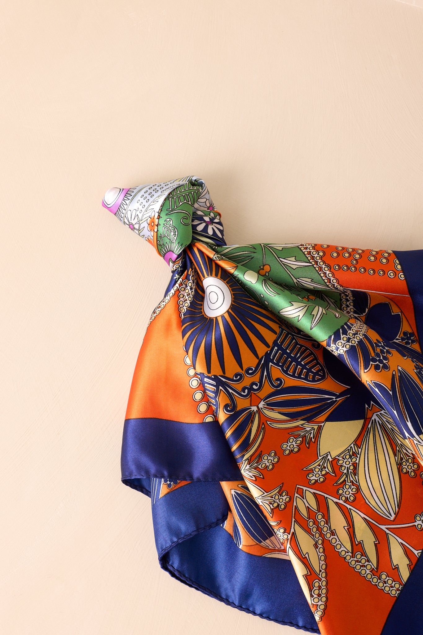 Square orange scarf with floral and four-leaf clover print, knotted in a stylish tie showing the glossy satin finish.