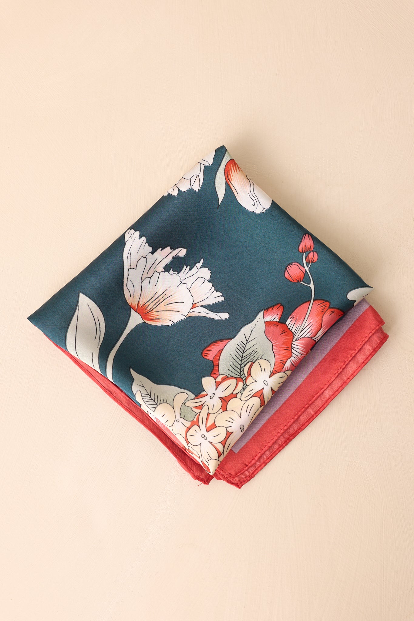 Square scarf neatly folded into a small compact square, displaying parts of the red and pink border trim and floral design on the shiny navy fabric.
