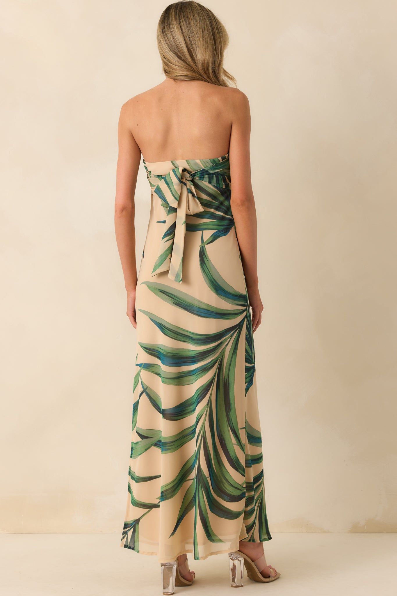 Rear view of the dress displaying the adjustable self-tie bow back and the continued flow of the palm print chiffon overlay over the beige lining.