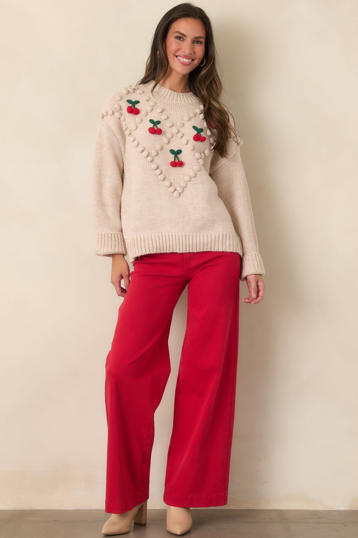 Model showing the relaxed fit of a beige cherry bobble knit sweater with a hip-length ribbed hem and roomy sleeves.
