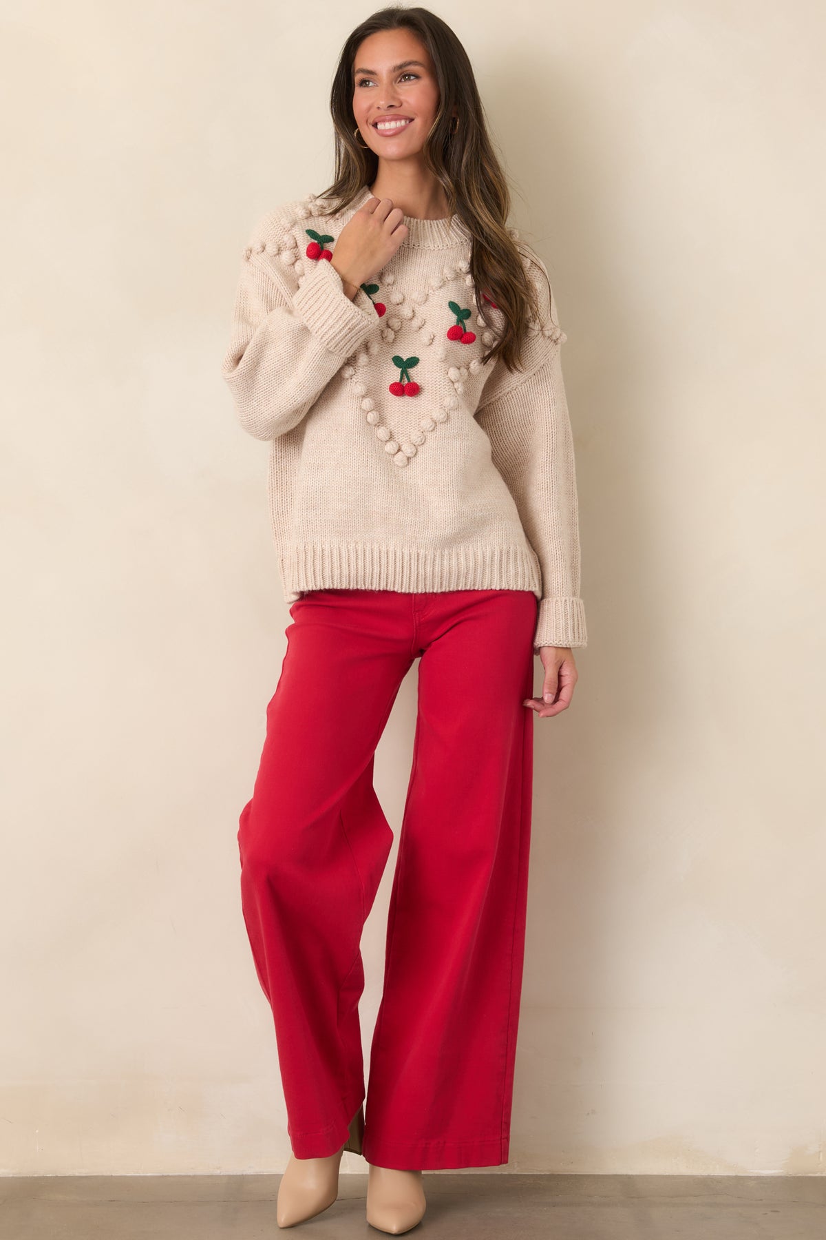 Beige cherry bobble knit sweater on a model with one arm raised, showing the roomy sleeve and wide ribbed cuff.