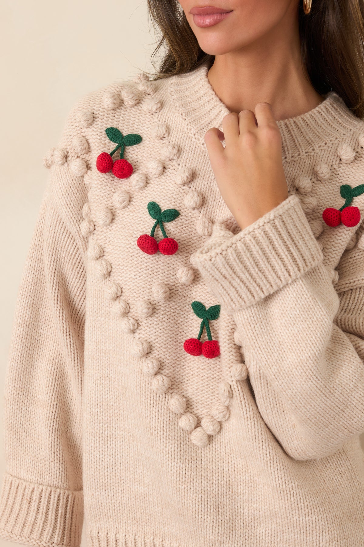 Close-up of raised red cherries, green stems and leaves, and beige diamond-pattern bobbles on the knit sweater.