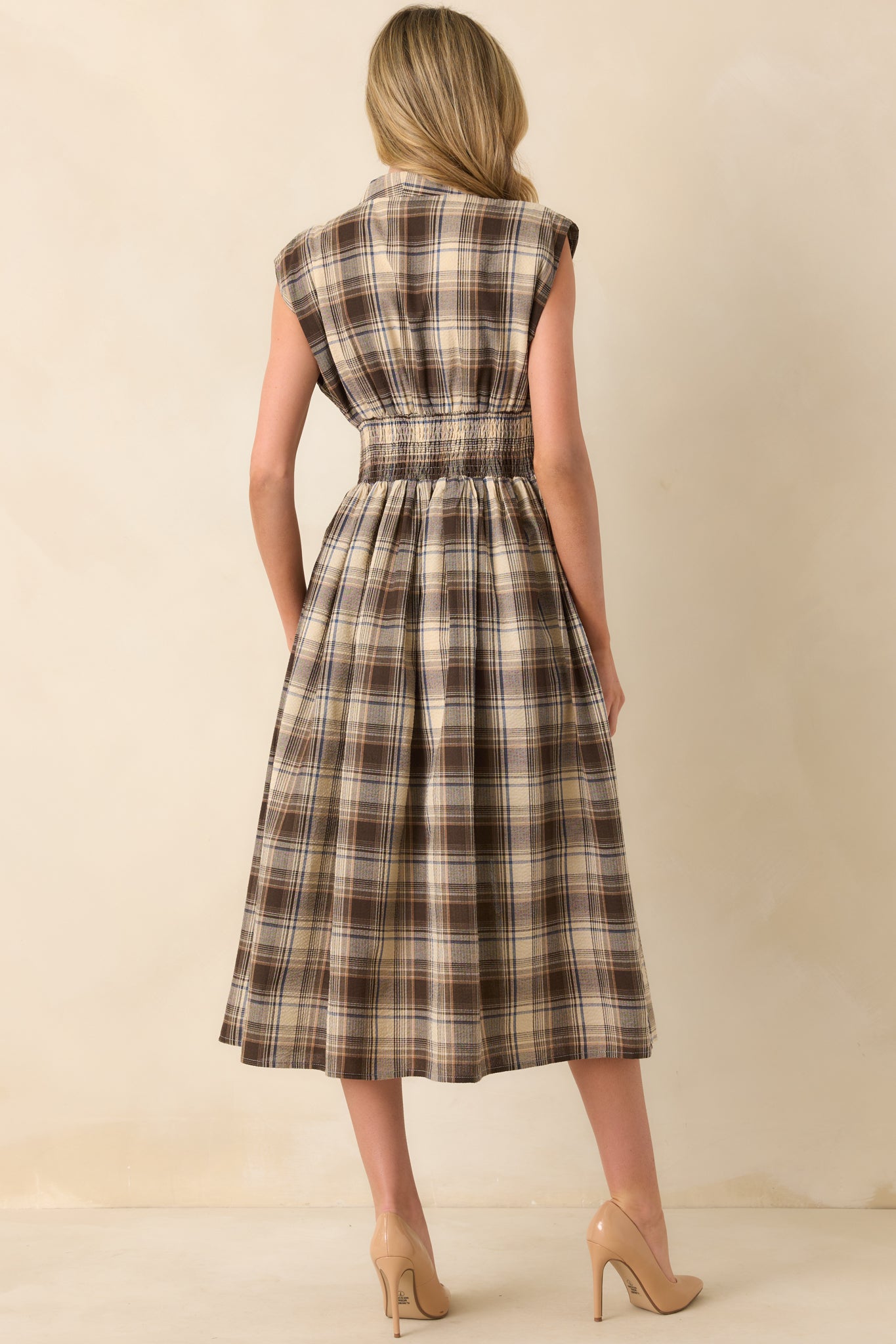 A view from behind showing the brown midi dress with capped sleeves, a smocked waist, and continuous plaid pattern.