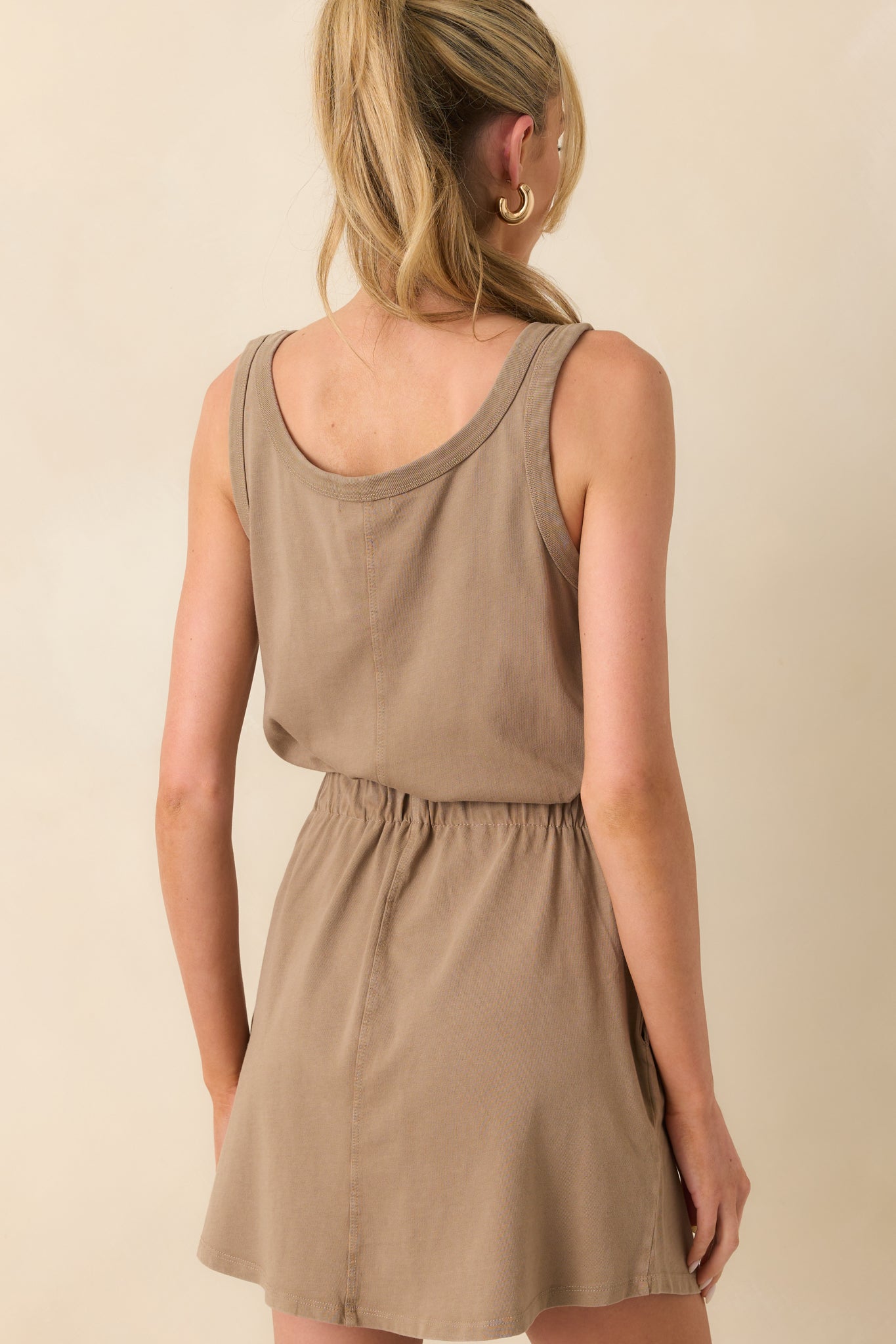 A view from behind of the tan dress showing the back of the straps, waistband fit, and overall mini dress length.