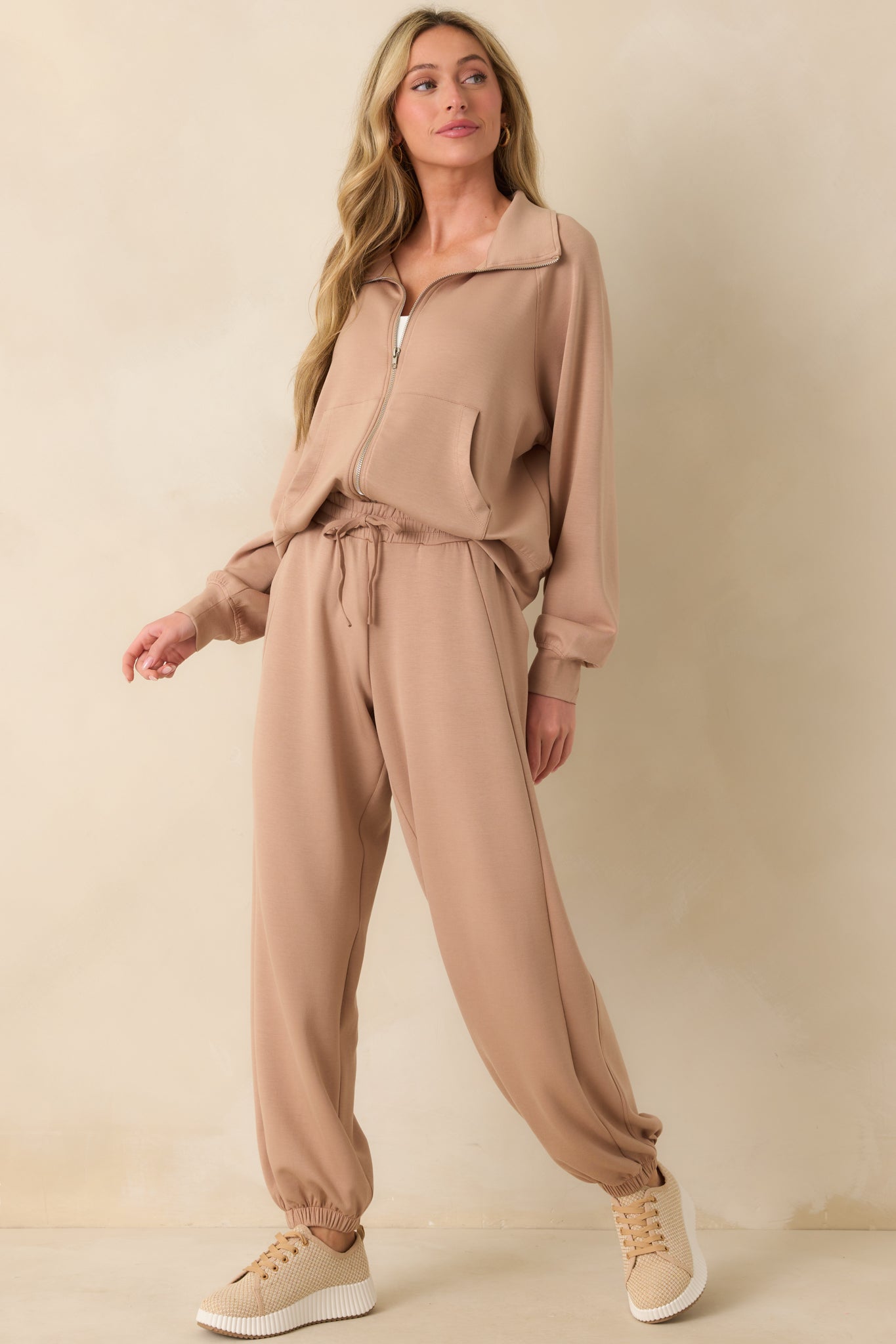 A full body front view showing the tan joggers’ thick elastic waistband, self-tie drawstring, and cuffed ankles.