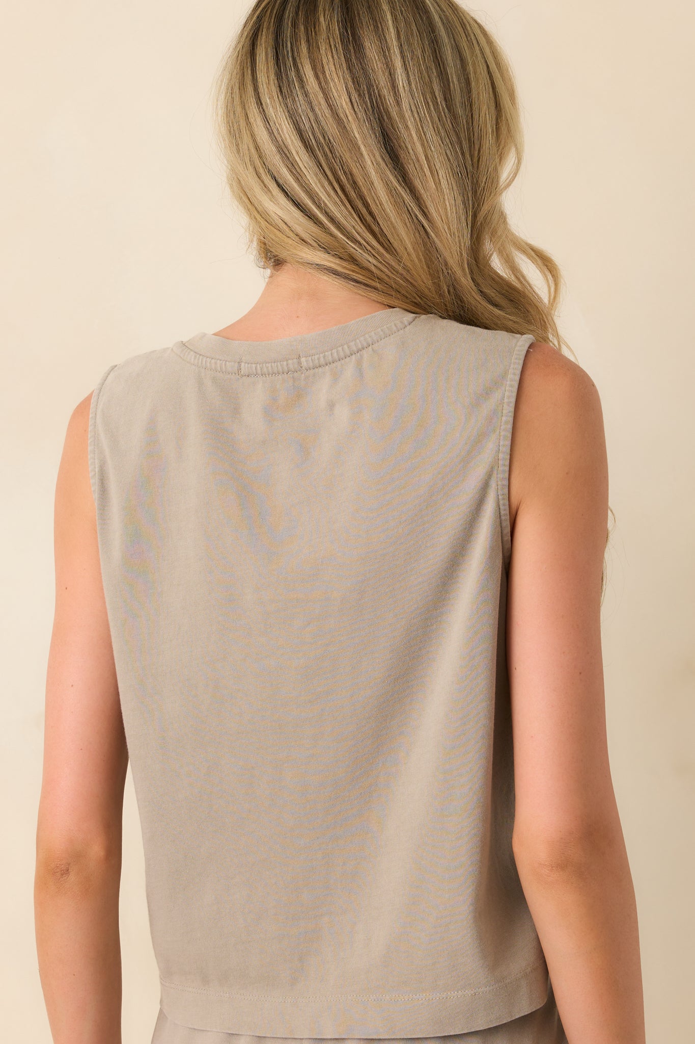 A back view of the taupe top displaying the continuation of the crew neckline, sleeveless cut, and slightly cropped silhouette.