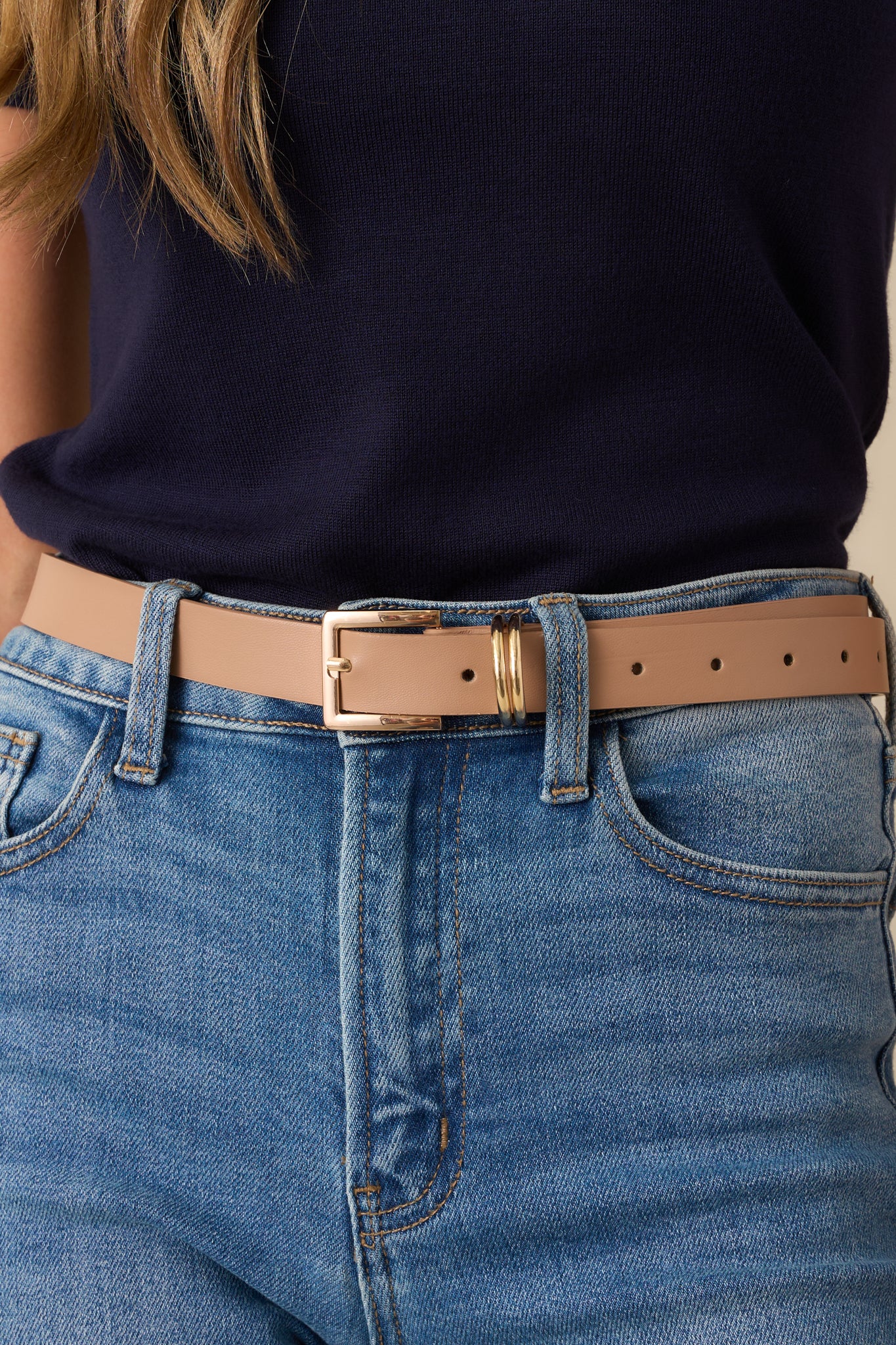 Zoomed-in image focusing on the gold-tone buckle, metal loops, and the evenly spaced punched holes on the beige faux leather.