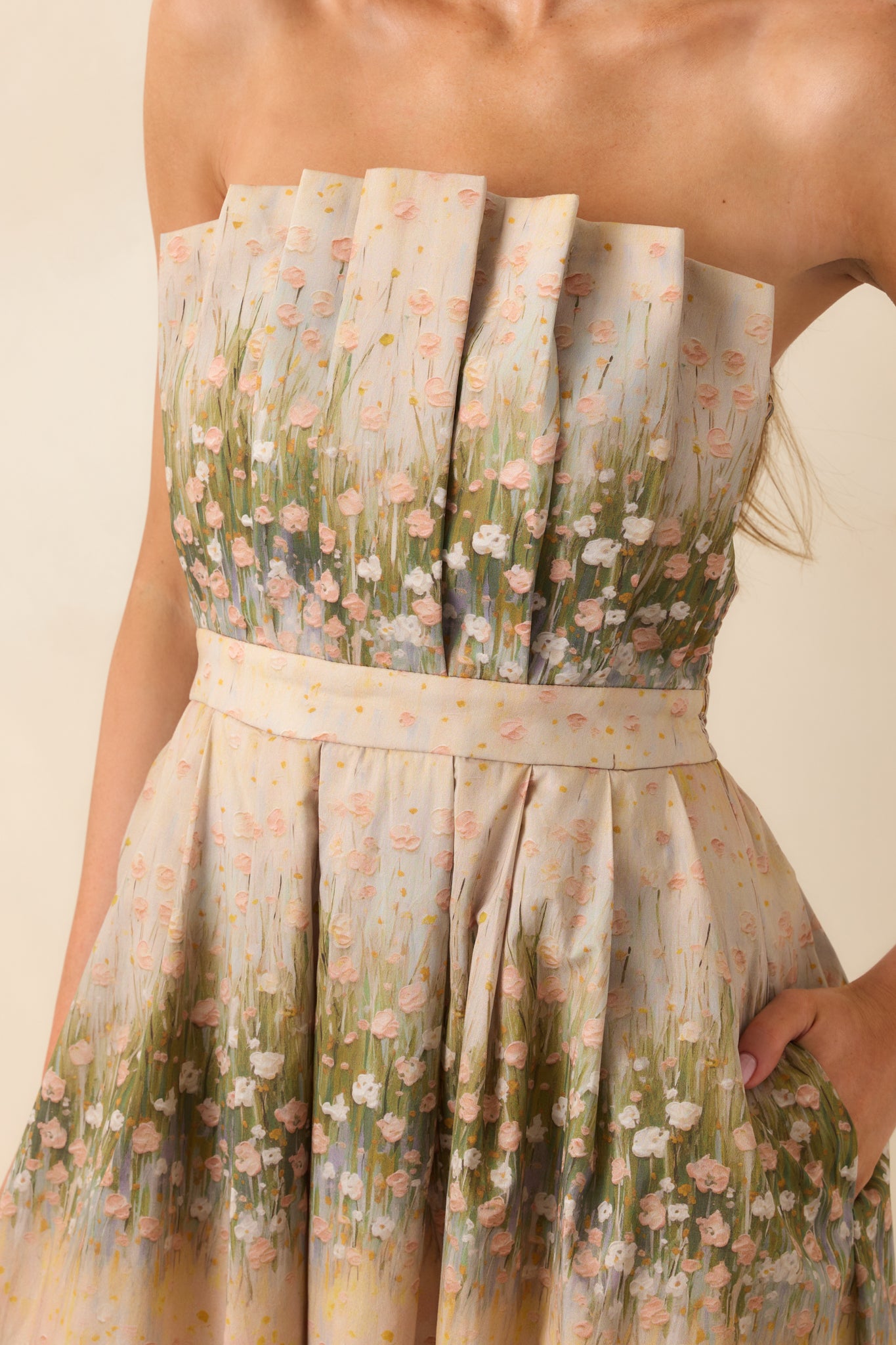 A close-up of the pleated bodice showing the green floral print on the beige fabric and fine stitching.