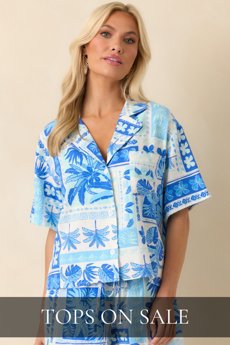 Model wearing a blue tropical print button-front top with statement earrings, styled in a studio setting. Top is featured in All Tops On Sale Shop.