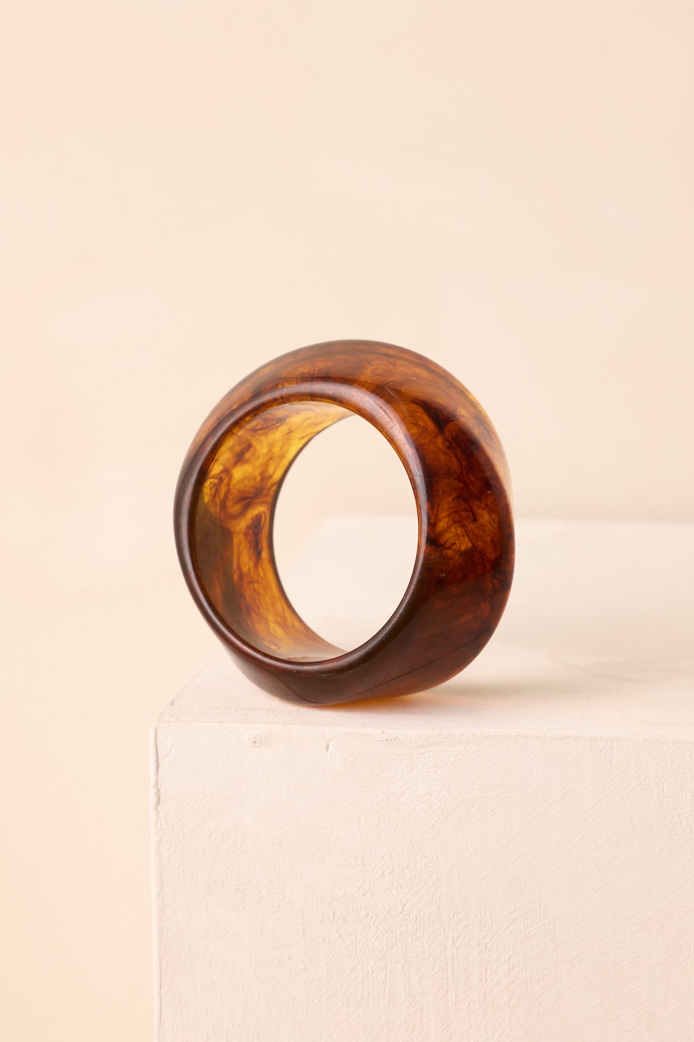 An angled view on a beige background showcasing the thick bangle silhouette and glossy surface.