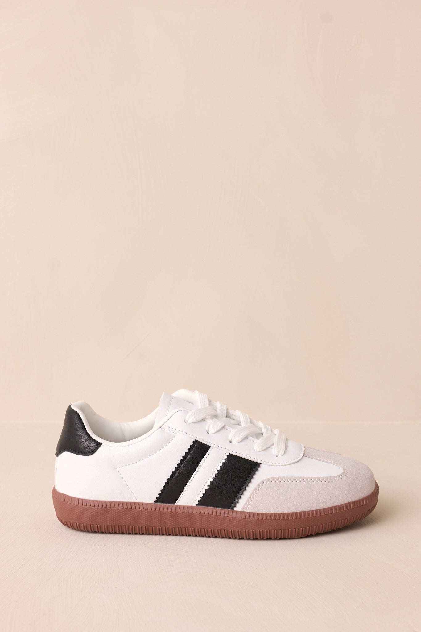 A side view of the white sneakers, highlighting the black faux leather stripes and sleek white faux leather material.