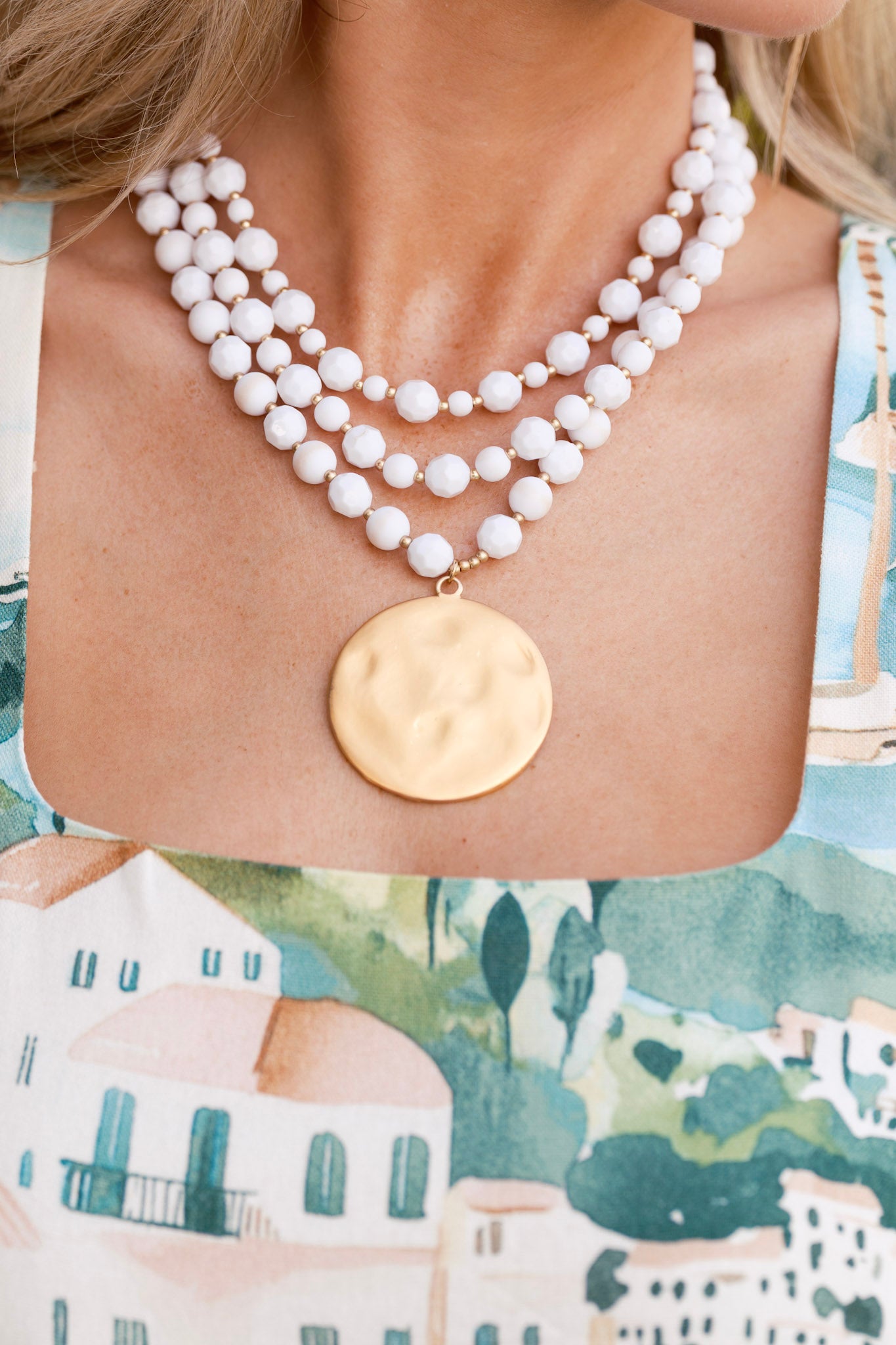 Close-up photo of necklace with beads alternating along the layered chains, gold hardware, and a hammered matte gold disc pendant.