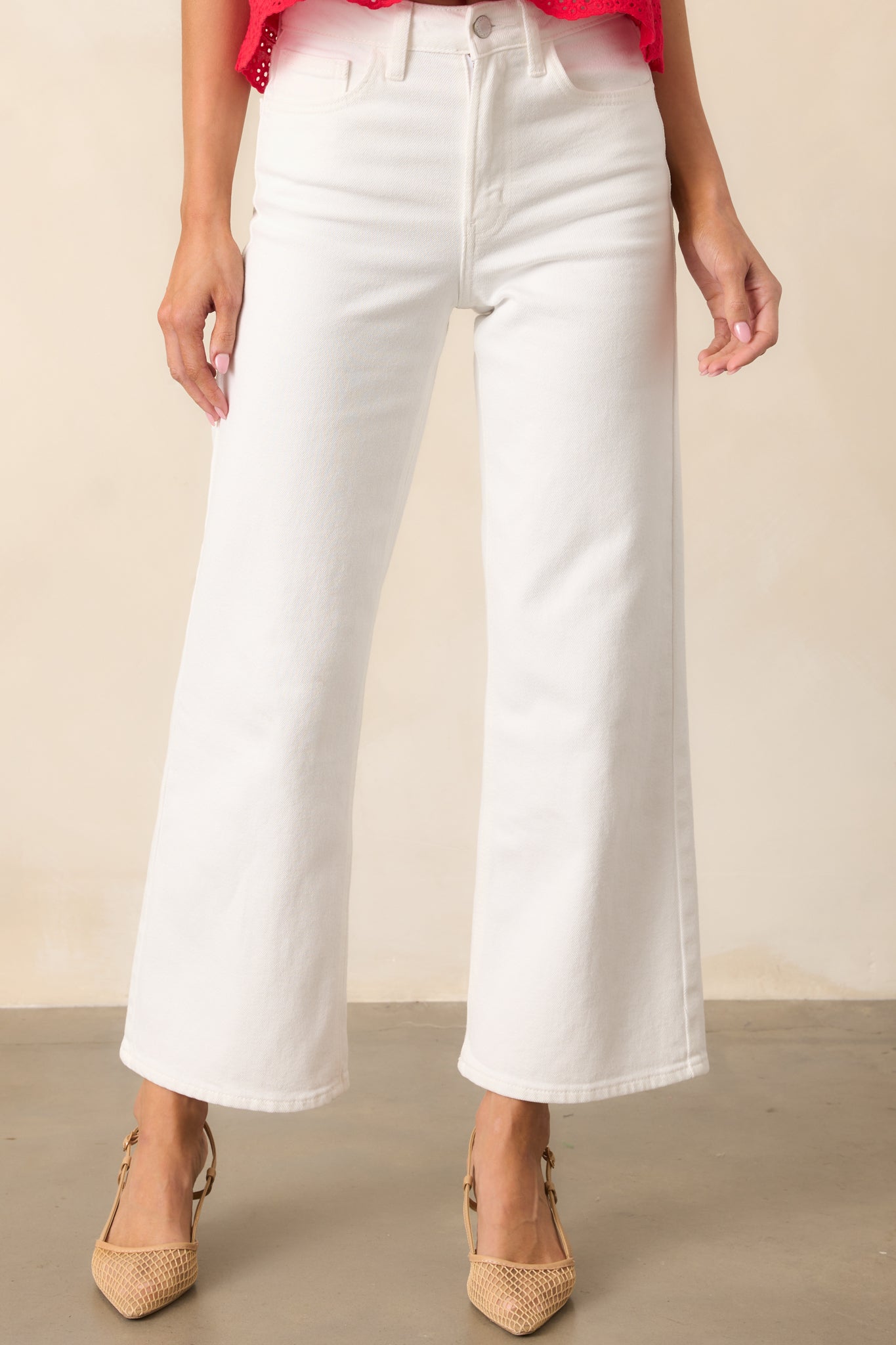 A closer look at the white high-waisted jeans, showing the button and zipper closure, belt loops, and functional pockets. The cropped length creates a clean, modern finish.