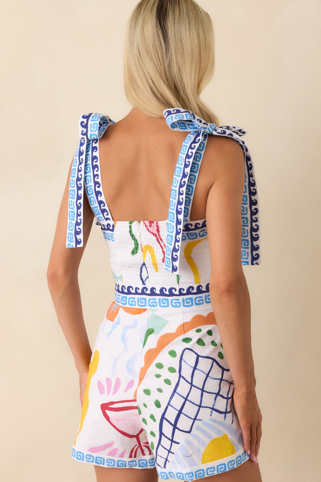Full back view of the romper highlighting the smocked back panel, tied straps, and the continuous multicolor Summer Spritz print.