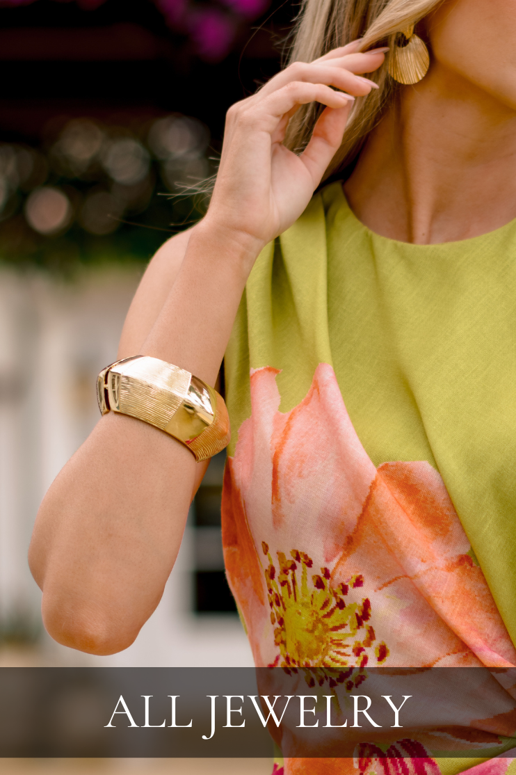 Close-up of model wearing gold statement jewelry, including a textured cuff bracelet and sculptural earrings, styled with a floral dress. Bracelet is featured in All Jewelry Shop.