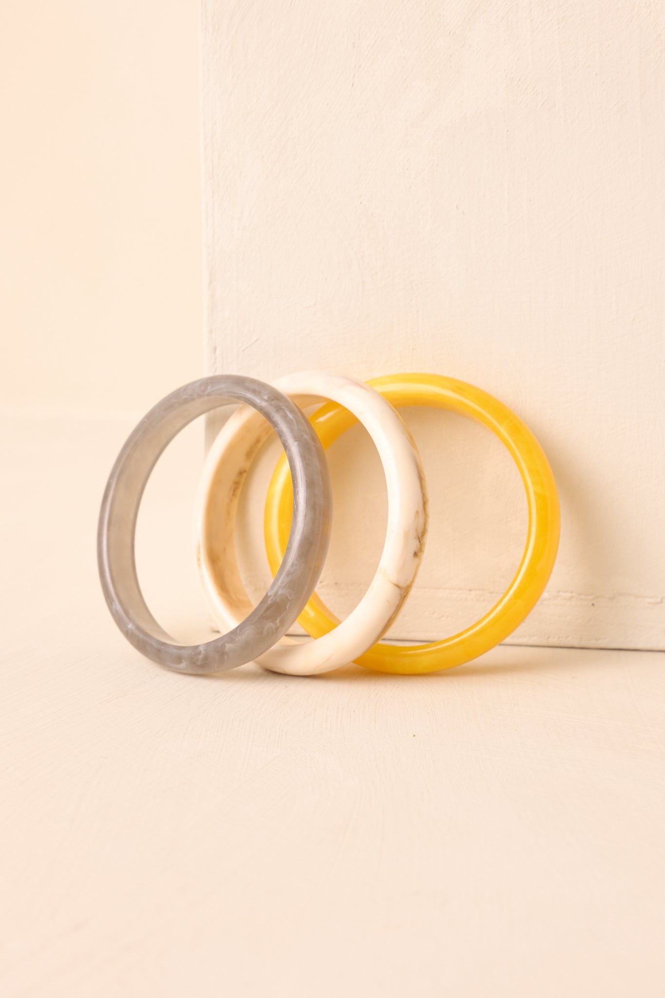 Yellow, ivory, and grey marbled bangle bracelets displayed on beige surface.