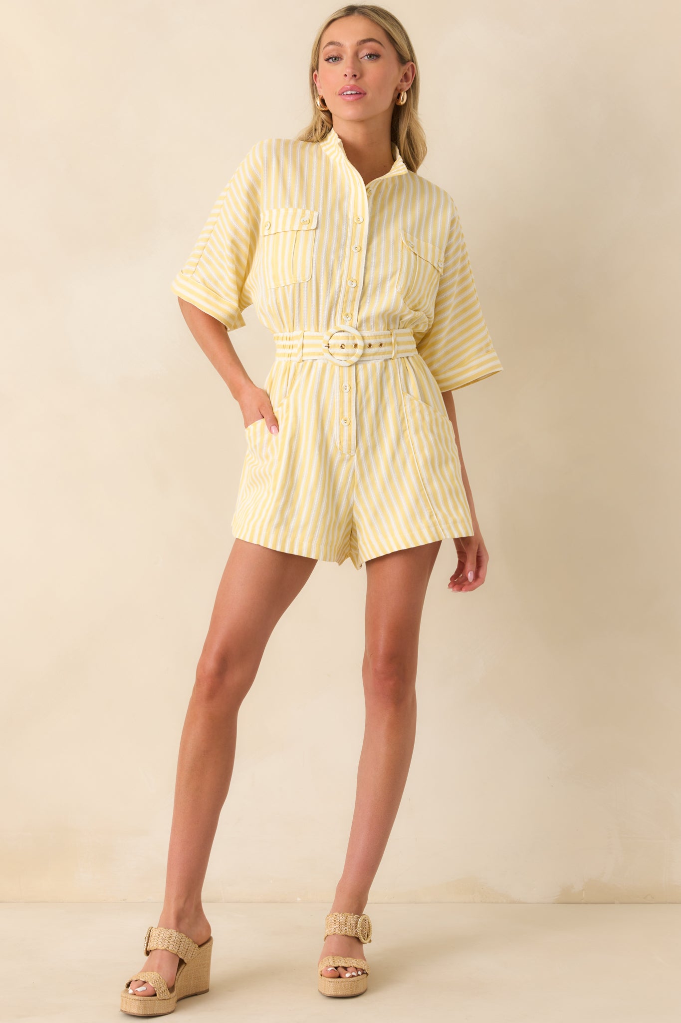 Full body of yellow striped romper featuring detailed stitching, collared neckline, button front, cuffed short sleeves, belted waist, and front patch pockets.