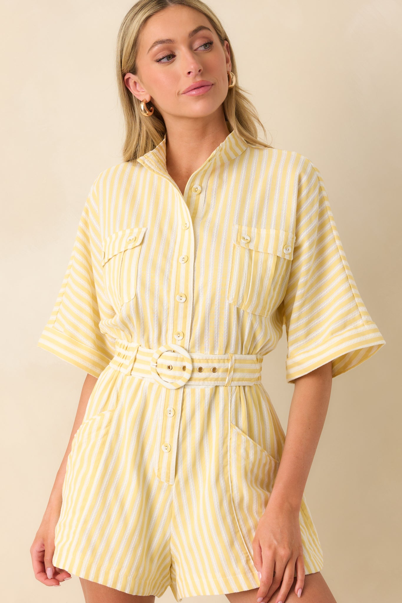 Close-up of Prosperina yellow striped romper featuring detailed stitching, collared neckline, button front, cuffed short sleeves, belted waist, and front patch pockets.