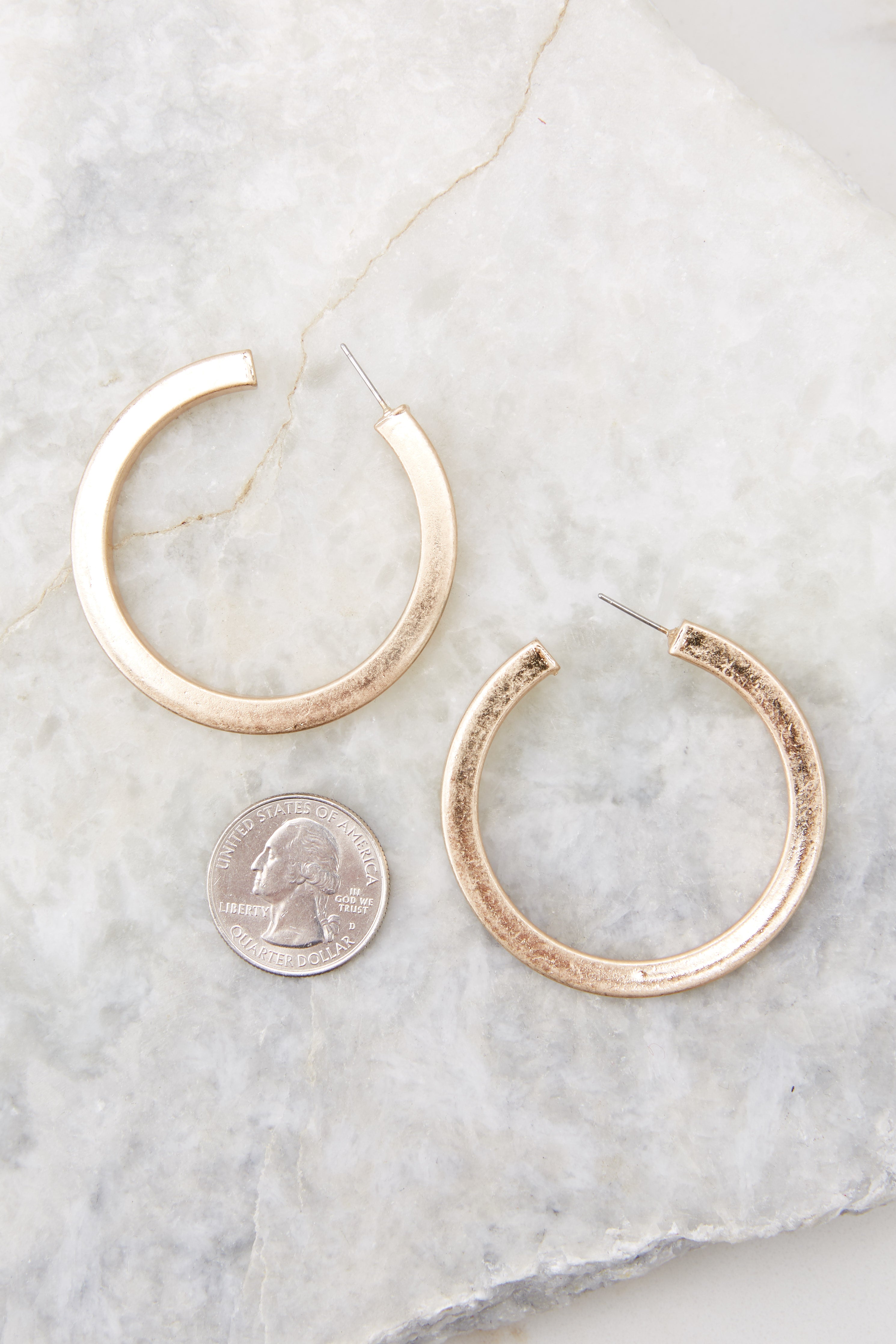 Overhead close up view of chunky gold hoop earrings compared to the size of a quarter.