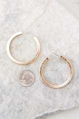 Overhead close up view of chunky gold hoop earrings compared to the size of a quarter. 