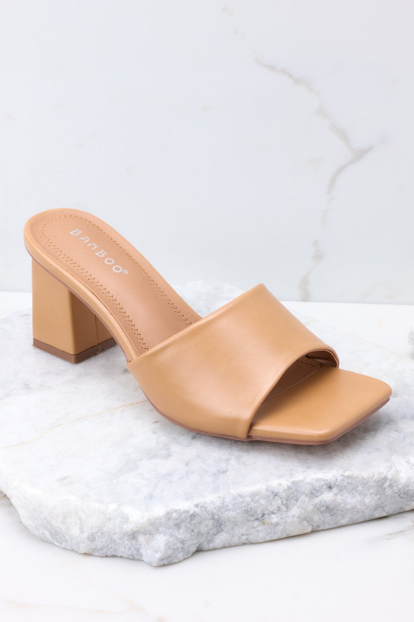 Close up view of these heels that feature a square toe, a thick strap across the top of the foot, a square heel, a faux-leather finish , and a slip-on design.