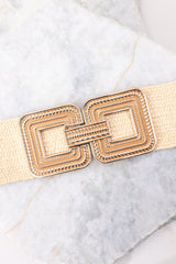 Close up view of this belt that features a square buckle with a hook closure, an elastic stretch woven material, and gold hardware.