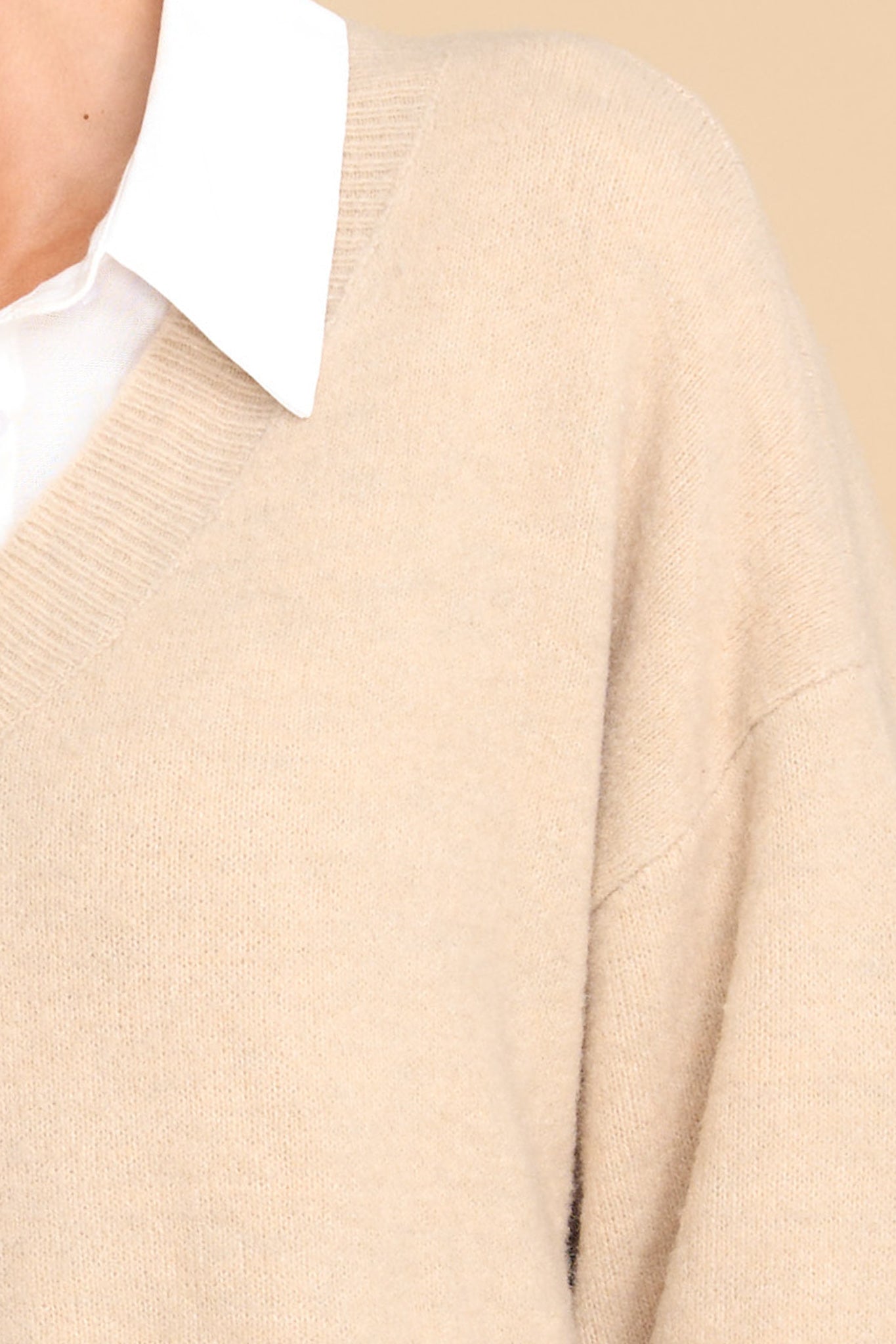 Close up view of this sweater that features a v-cut neckline, long sleeves, and a ribbed waistband.