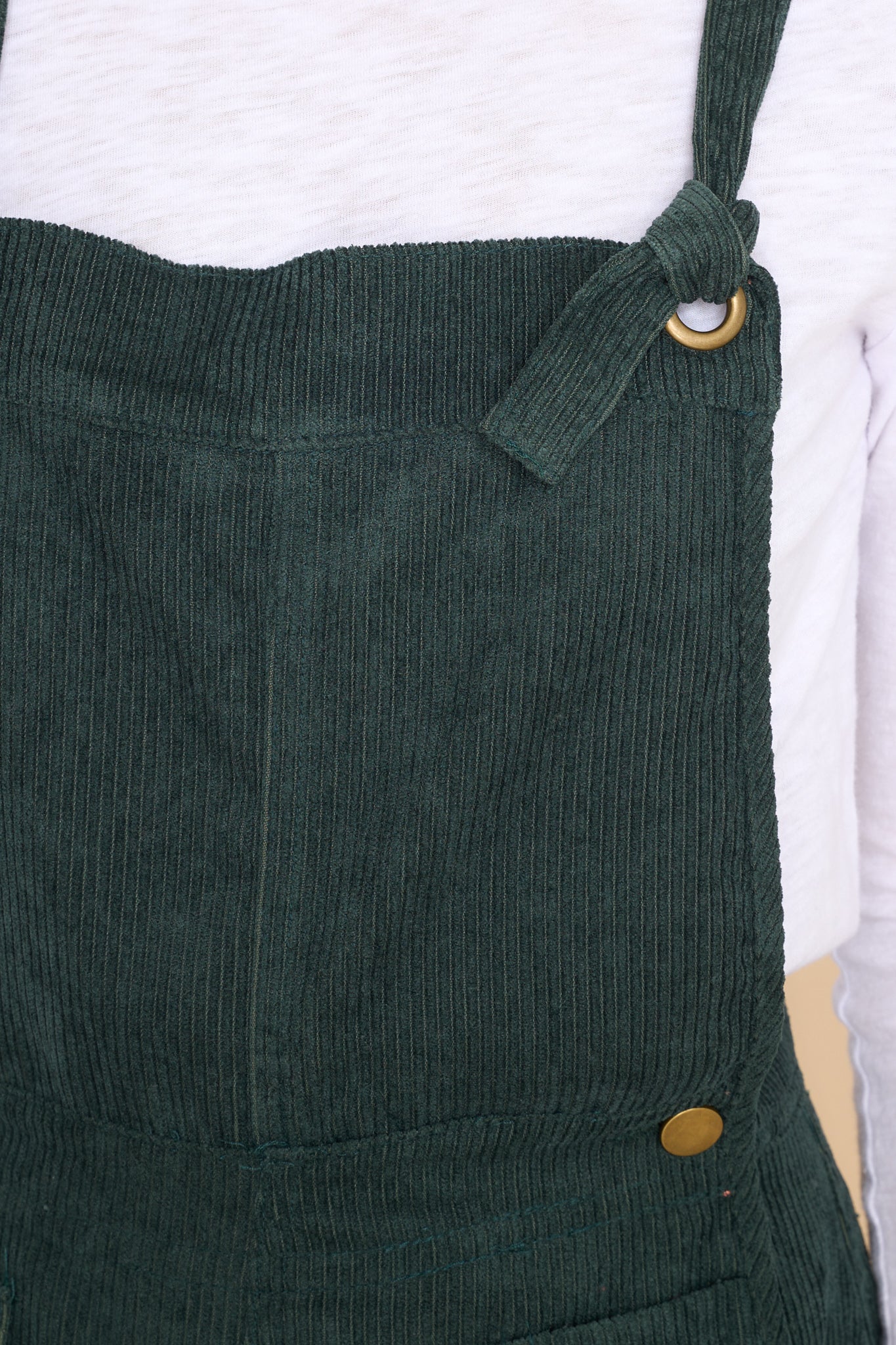 Close up view of these overalls that feature adjustable self-tie straps, buttons below the bust to allow for a folded look, and a corduroy texture throughout.