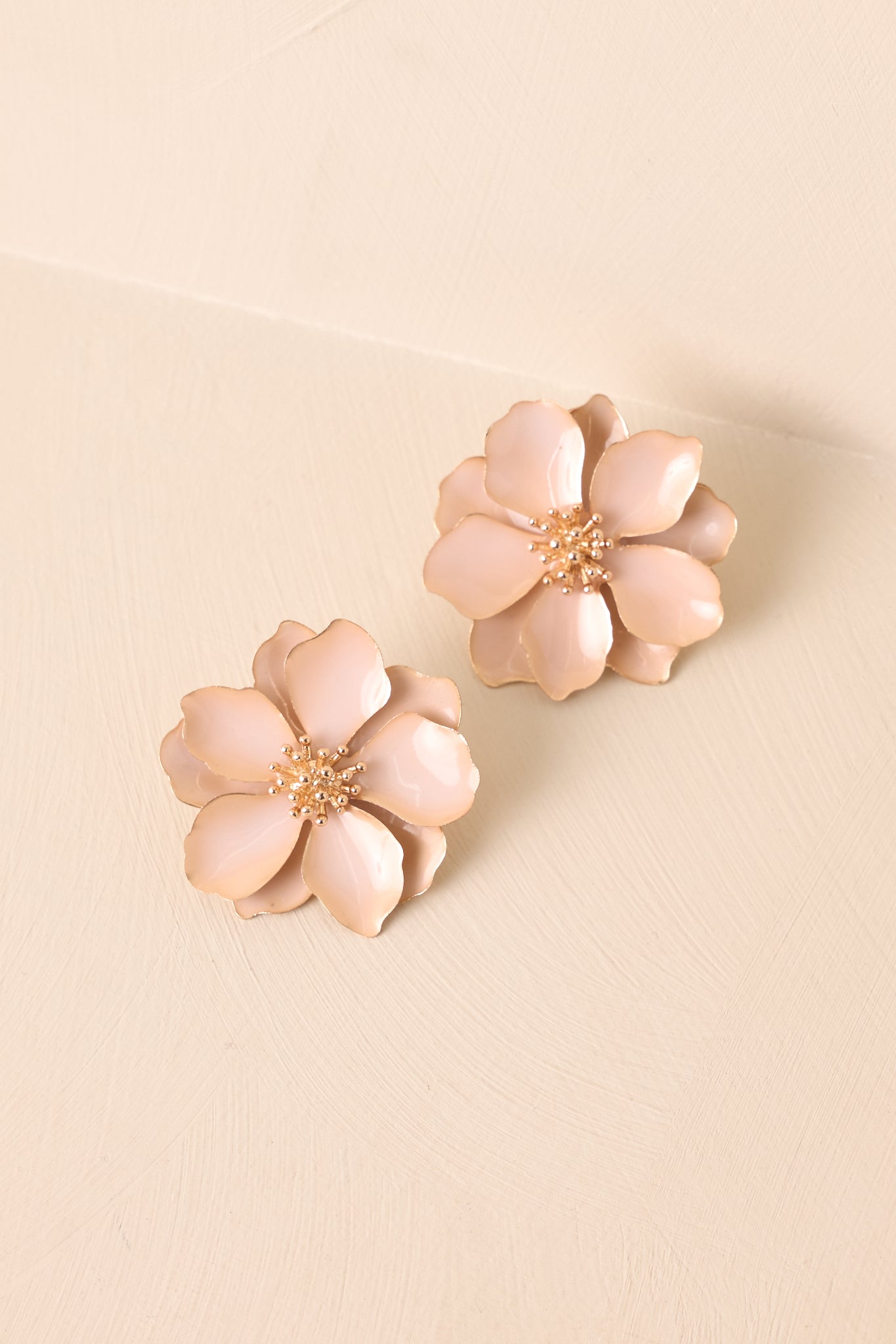 Beige flower petal earrings with gold textured centers displayed on beige backdrop.
