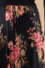 Close up view of this dress that features a pleated floral print satin like skirt in shades of orange, pink, and green.