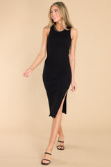 This black dress features a U-neckline, a slit in the left side reaching the mid-thigh, a bodycon silhouette, and a soft ribbed material throughout.
