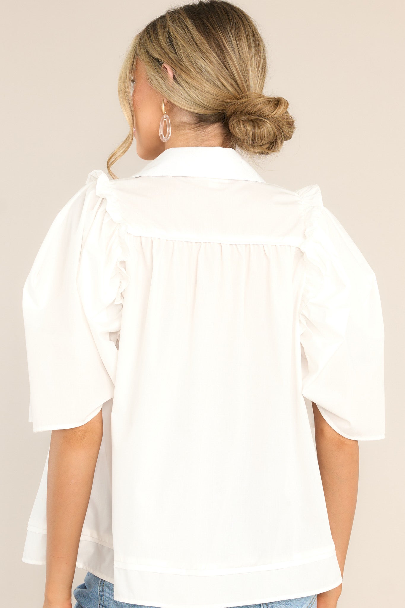 Back view of this top that features a collared neckline, functional buttons down the front, butterfly short sleeves, and ruffle detailing.