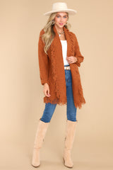 This rust colored cardigan features a folded neckline, fringe detailing, and long sleeves with ribbed cuffs.