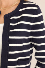 Close up view of this white and blue cardigan features a round ribbed neckline, long sleeves with ribbed cuffs, ribbed hemline, and a modern horizontal striped pattern.