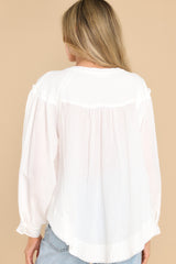 Back view of this top that features a round neckline, wide sleeves with buttoned cuffs, functional buttons down the bodice, and an uneven, raw hemline.