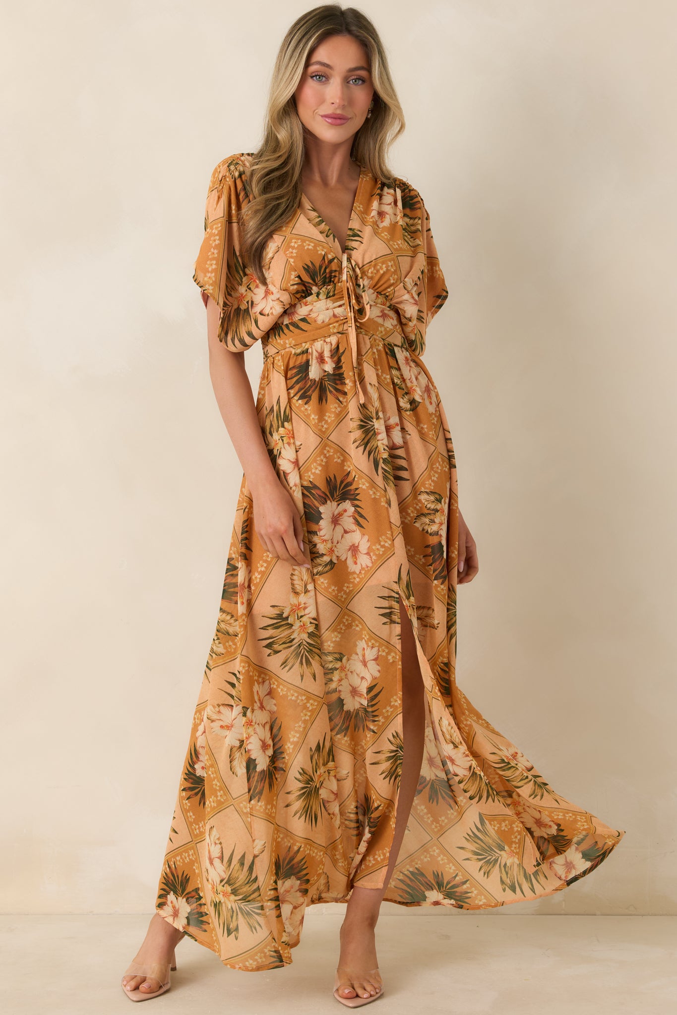 Front view of a peach tropical print maxi dress with V-neckline, flutter sleeves, and flowing skirt.