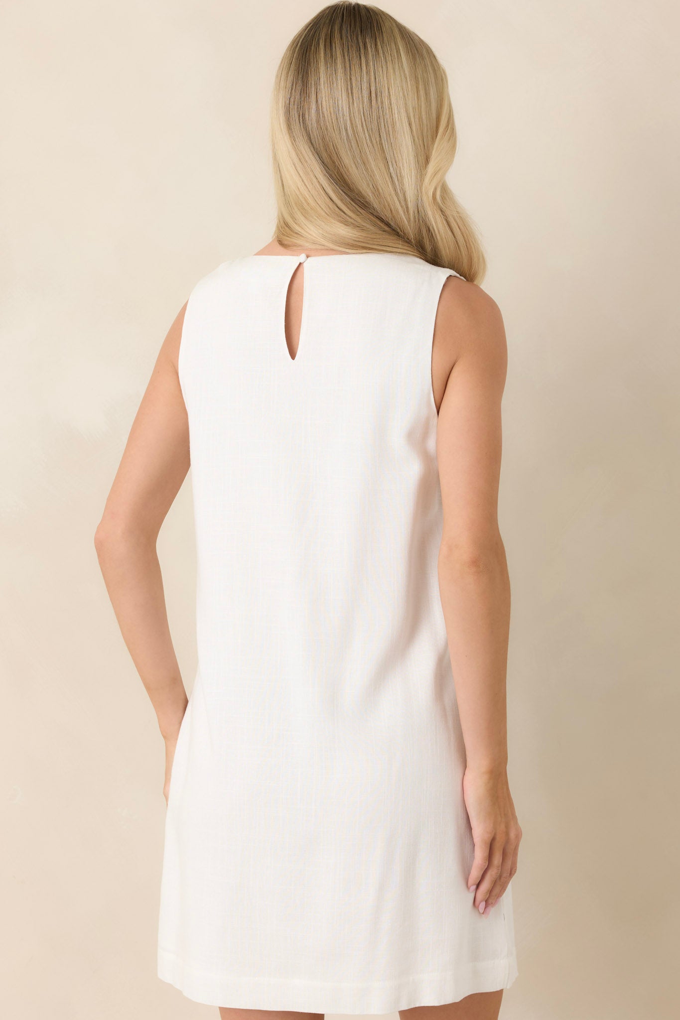 Woman wearing a white sleeveless dress against a beige background