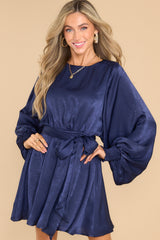 Front view of this dress that features a round neckline, a keyhole with a button closure on the back, flowy sleeves with smocked cuffs, an elastic waistband, a self-tie, and a flowy skirt.