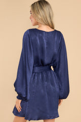 Back view of this dress that features a round neckline, a keyhole with a button closure on the back, flowy sleeves with smocked cuffs, an elastic waistband, a self-tie, and a flowy skirt.