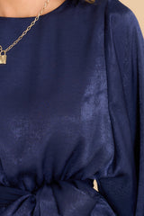 Close up view of this dress that features a round neckline, a keyhole with a button closure on the back, flowy sleeves with smocked cuffs, an elastic waistband, a self-tie, and a flowy skirt.