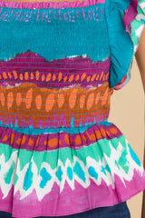 Close up view of this top that features a square neckline, flutter sleeves, a smocked bodice, ruffle detailing at the hips, and a vibrant pattern throughout.