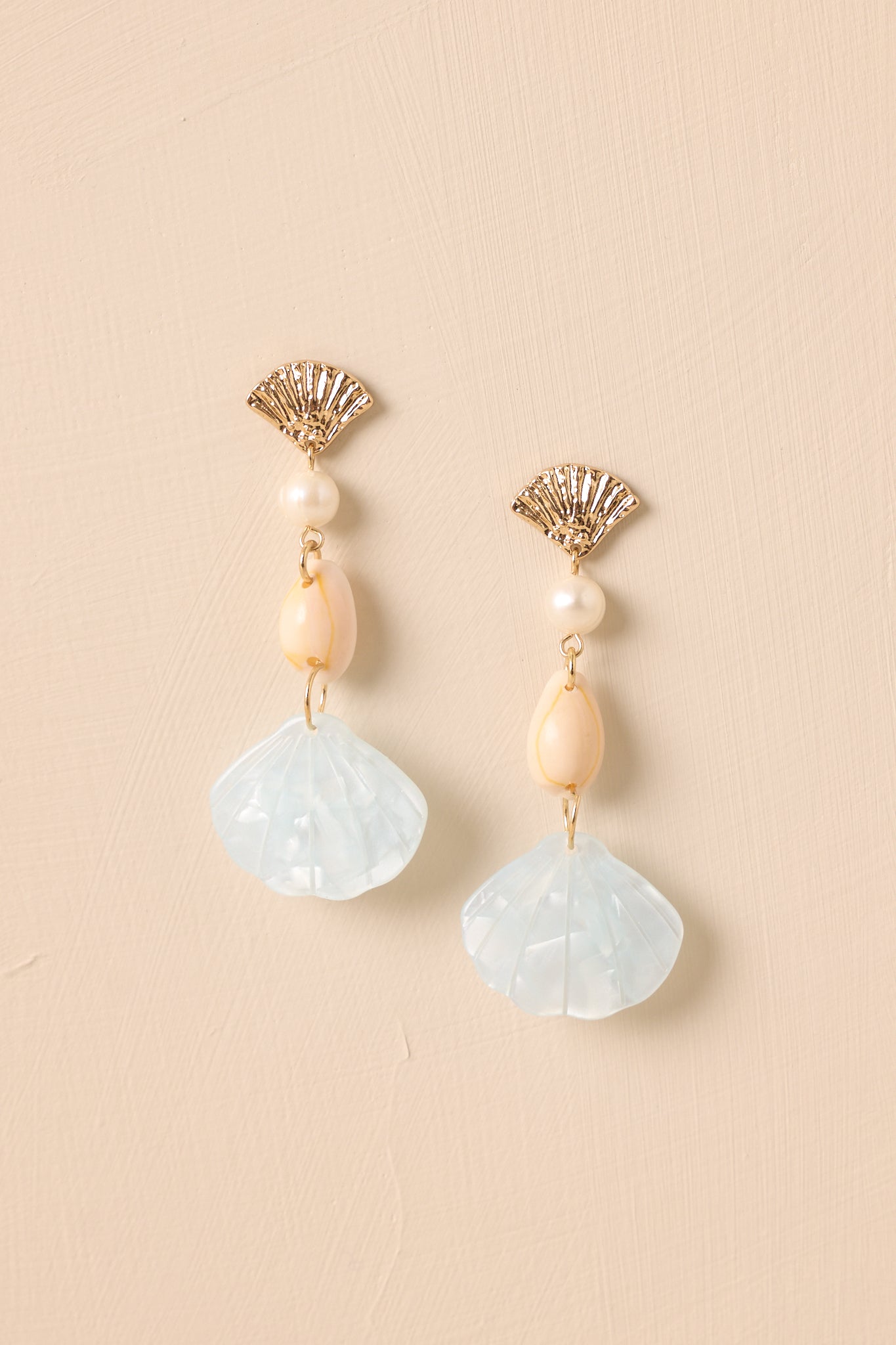 Pair of earrings showing gold seashell stud, ivory charms, and light blue pearlescent drop.