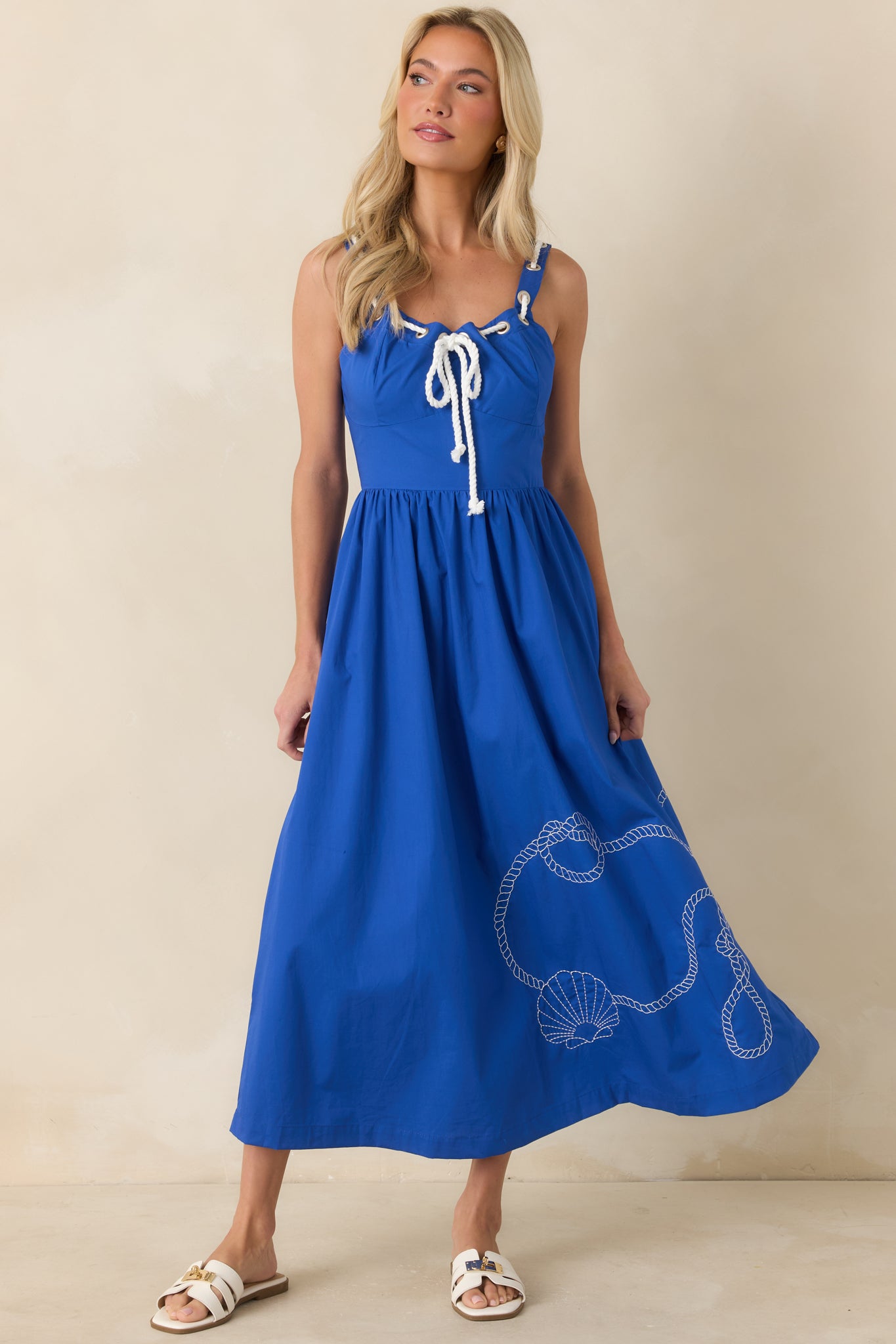 Embroidered blue midi dress with nautical-inspired rope detailing, functional pockets, and soft movement throughout the skirt.