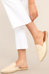 Side view of sandals that feature a pointed toe, slip-on design, and a cream, woven detail on the top. 