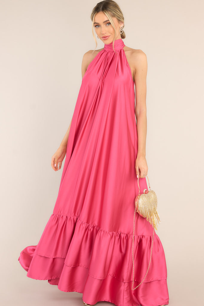 This floor length hot pink dress features a halter neckline with a self adjustable tie around the neck, a flowy long silhouette, and a tiered bottom. 