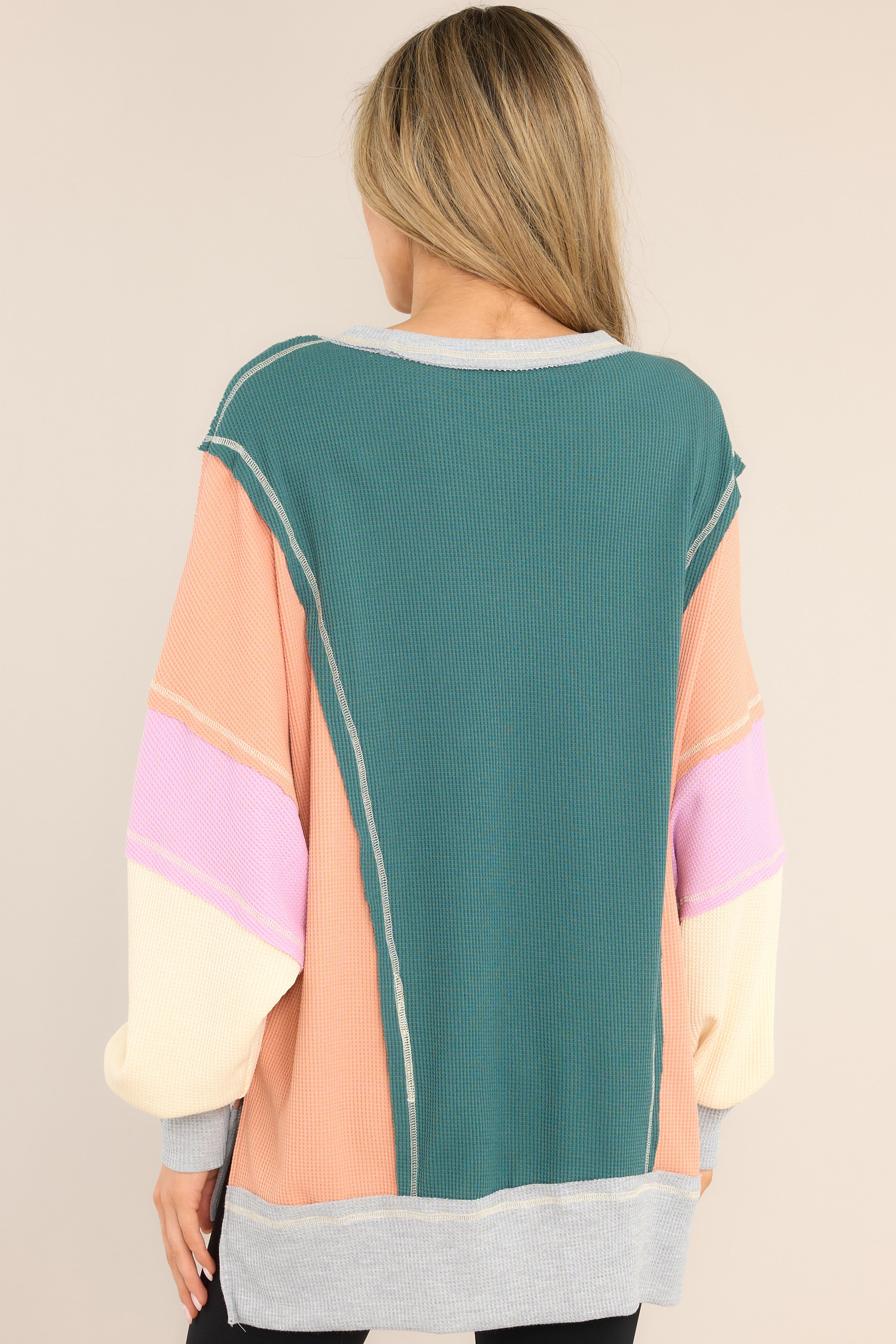 Back view of  this top that features a crew neckline, dropped shoulders, front pockets, a waffle knit material, cuffed sleeves, and a high-low split hemline.