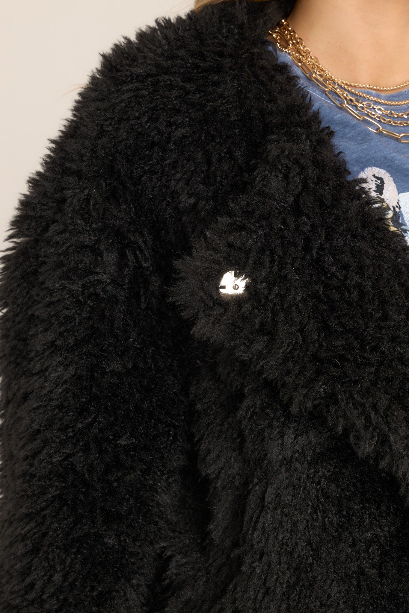 Close up view of this faux fur plush jacket that features a rounded neckline, elastic cuffs, two front waist pockets, and snap buttons with an asymmetrical closed front. 
