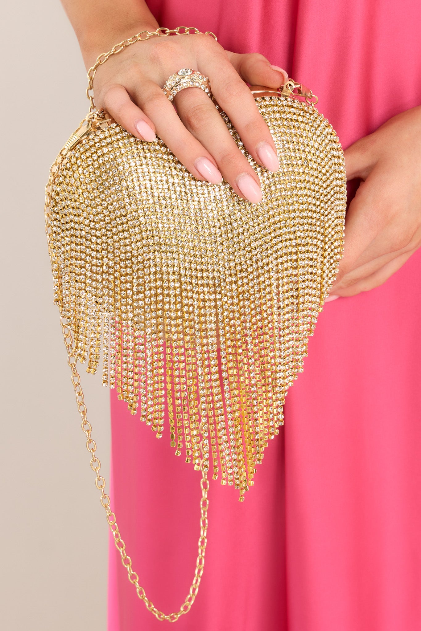 Close up view of this handbag that features gold hardware, rhinestone fringe, a removable chain strap, a ring like feature, and a snap closure.