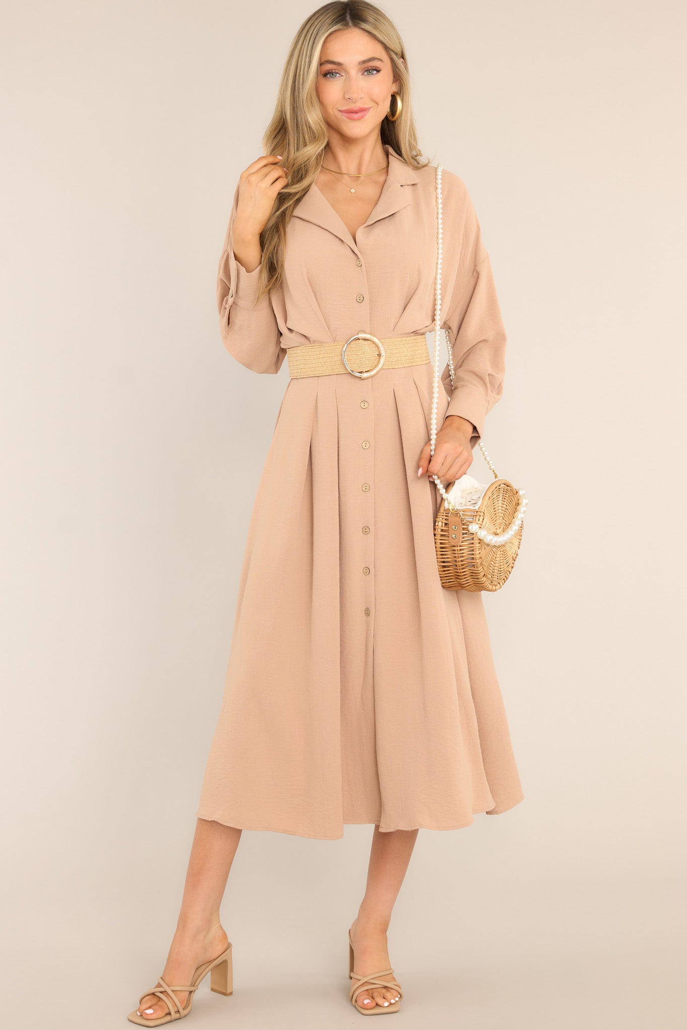 This beige midi dress features a collard neckline, functional buttons going down the front, long sleeves with button closures, and a pleated design at the waist.